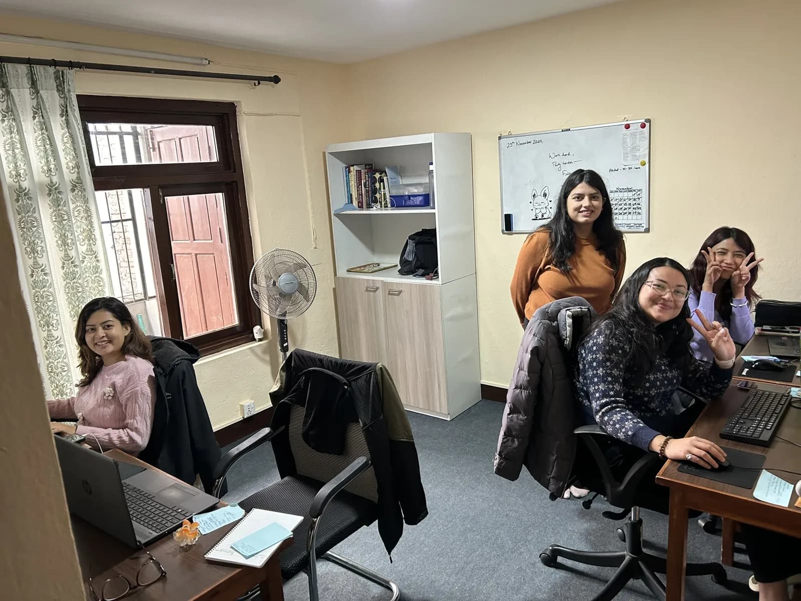 Three colleagues at desks in the corner room with a whiteboard